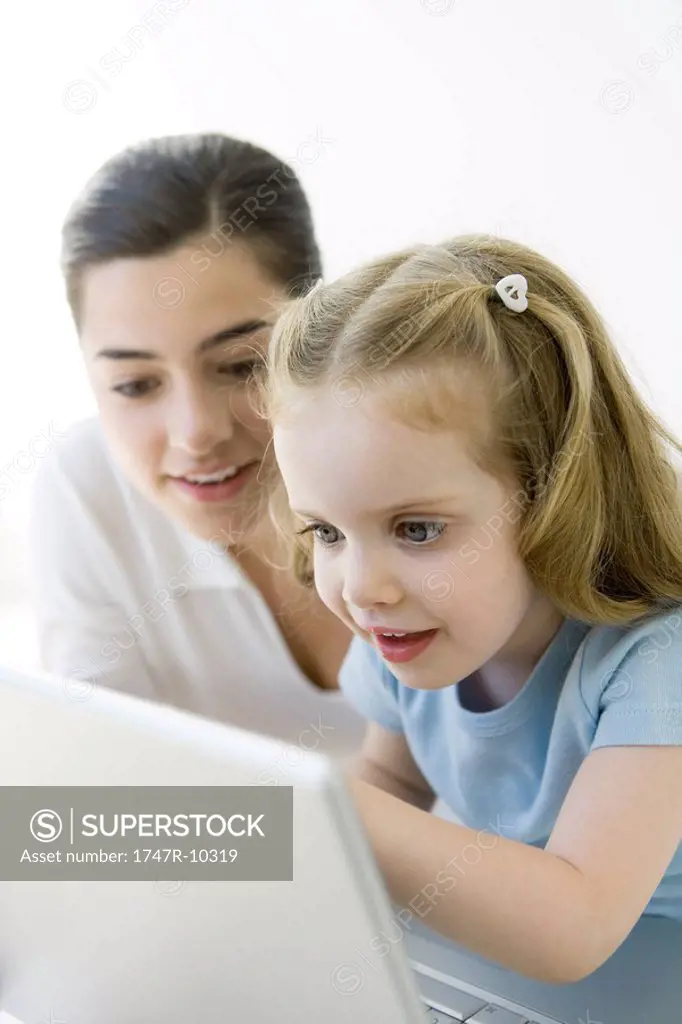 Mother and young daughter looking at laptop computer together, smiling