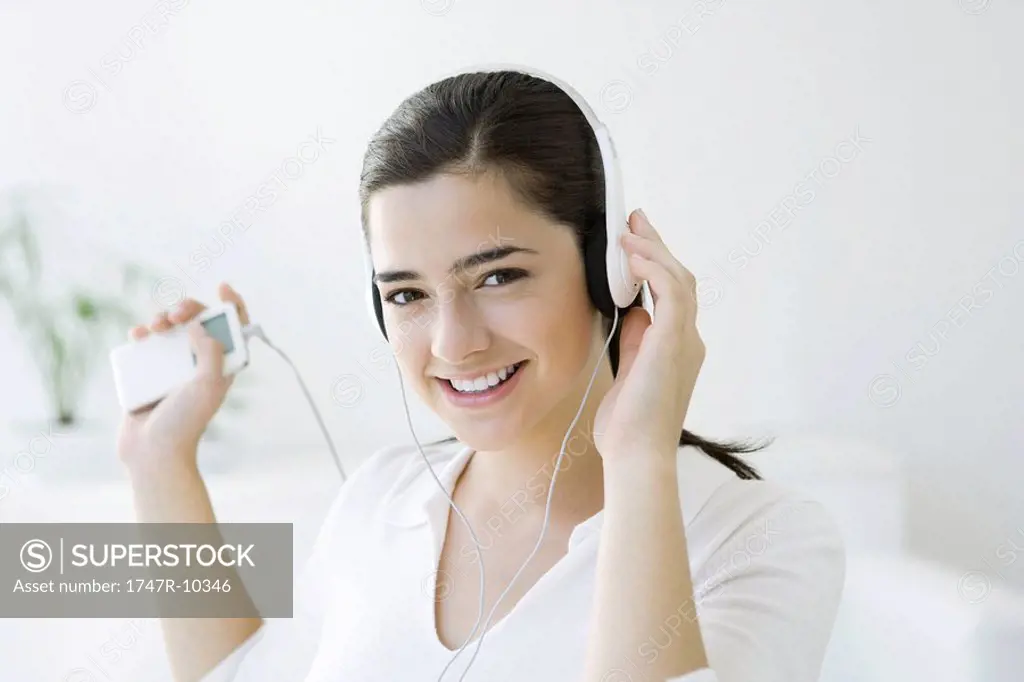 Woman listening to MP3 player with headphones, smiling at camera
