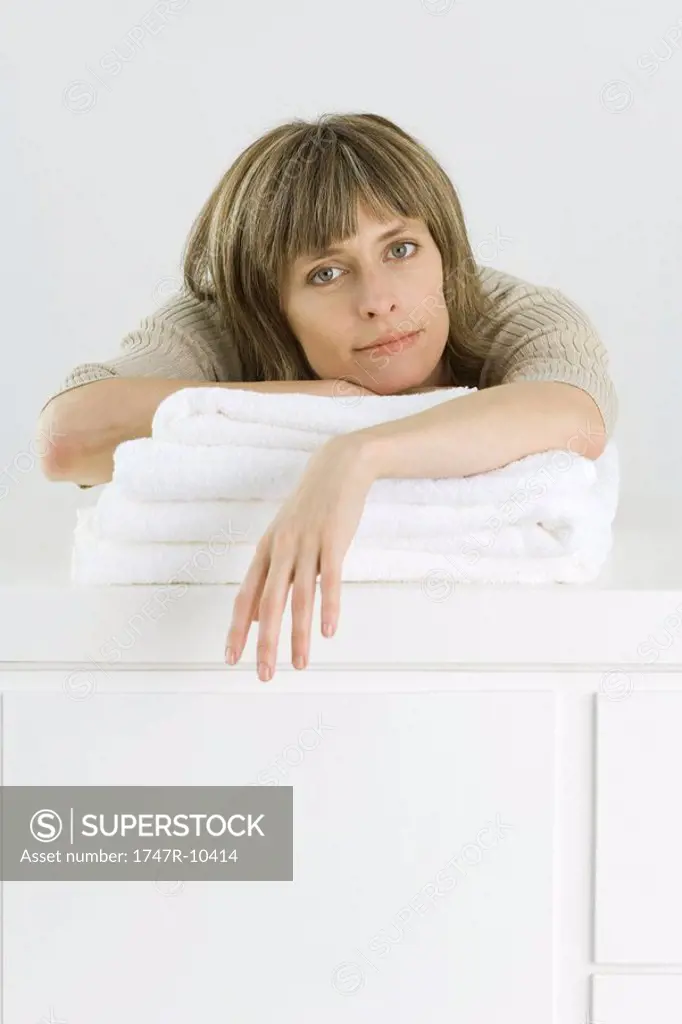 Woman leaning over stack of towels on counter, looking at camera
