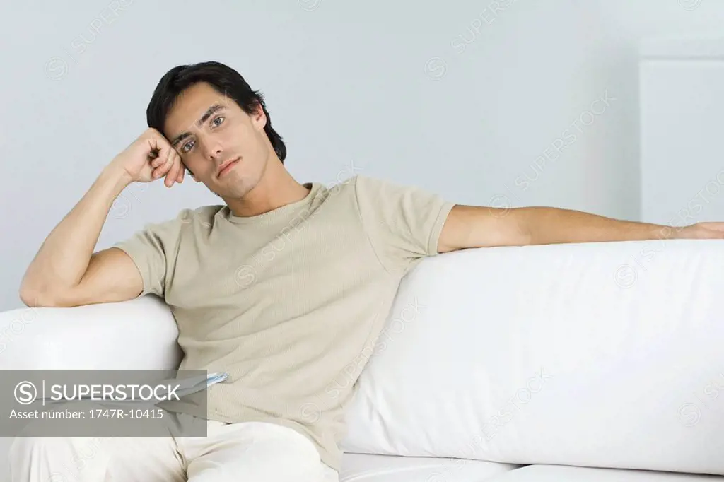 Man relaxing on sofa, looking at camera, leaning on elbow