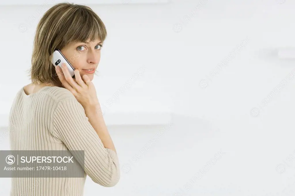 Woman using cell phone, smiling over her shoulder at camera
