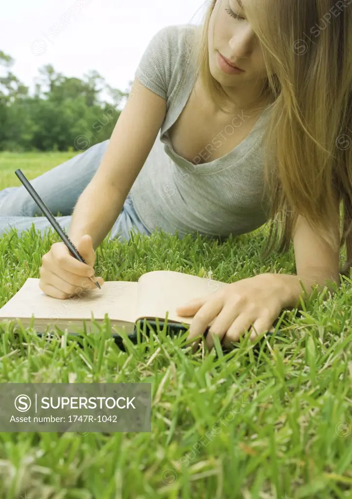 Young woman reclining in grass, writing in journal