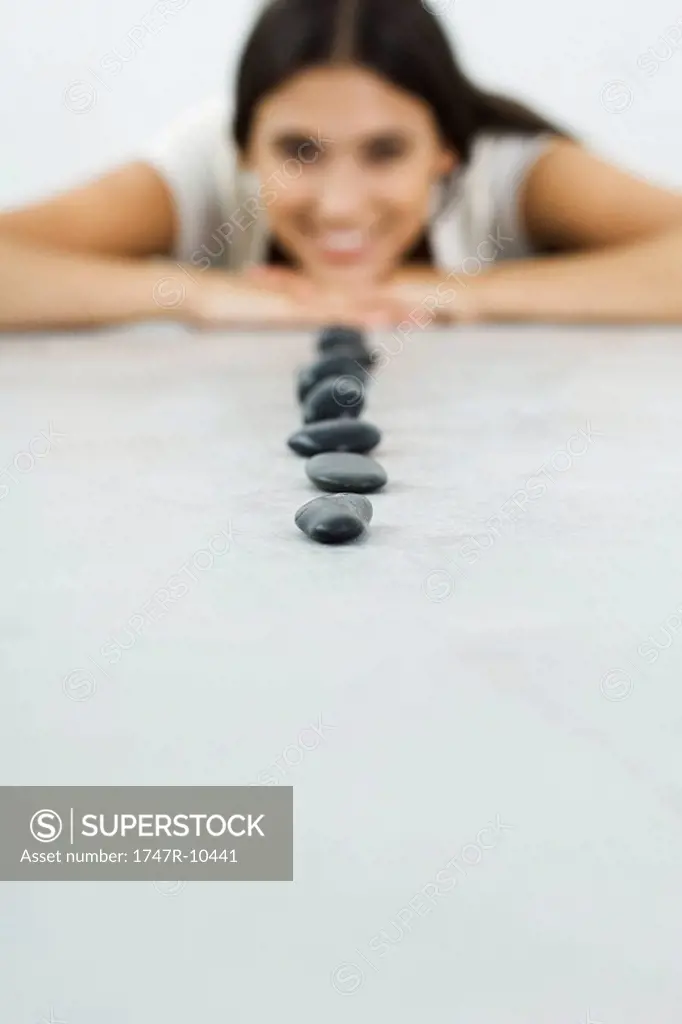 Small black stones in a line, woman lying on stomach resting head on arms in background