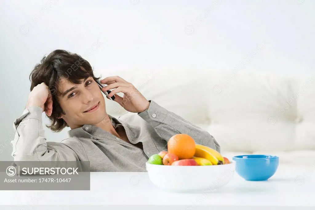 Man sitting at coffee table, using cell phone, smiling at camera