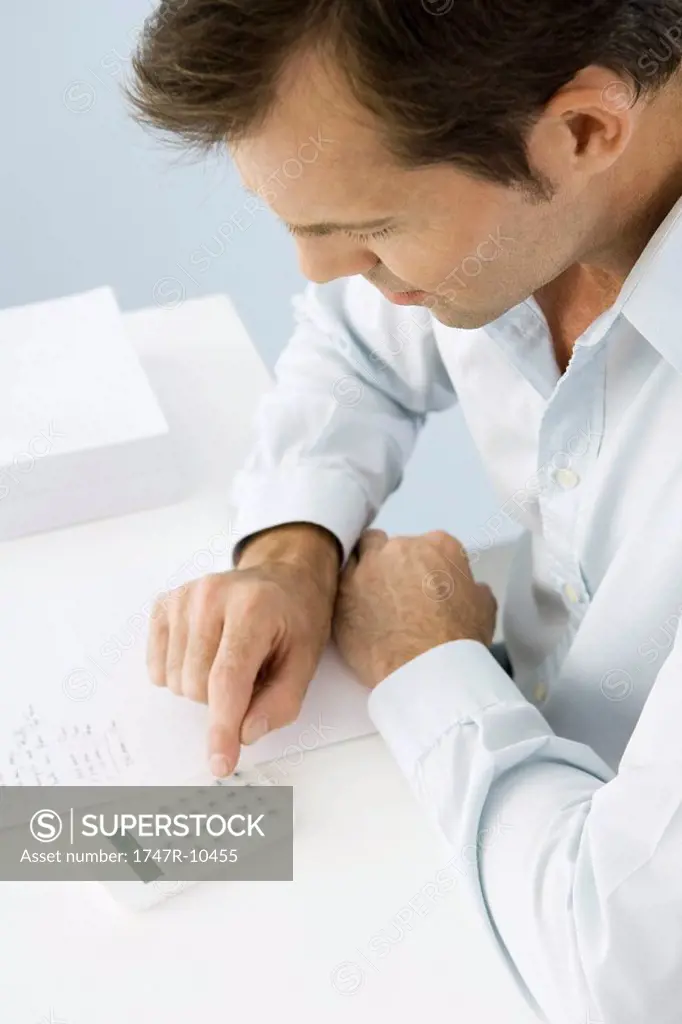 Man using calculator, sitting at table, high angle view