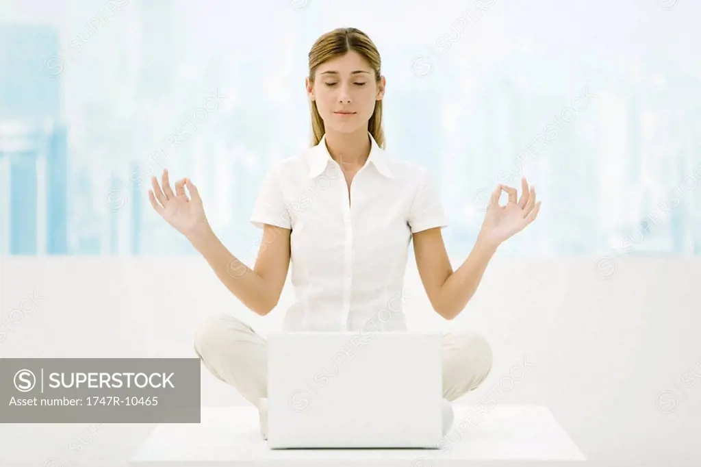 Woman sitting in lotus position in front of laptop computer, eyes closed