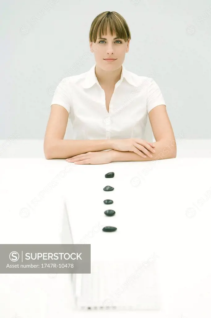 Woman sitting with arms folded, line of stones leading to laptop computer