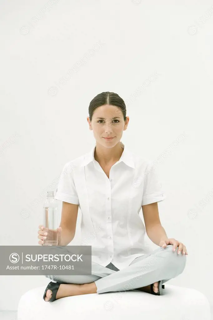 Woman sitting cross-legged, holding water bottle, smiling at camera