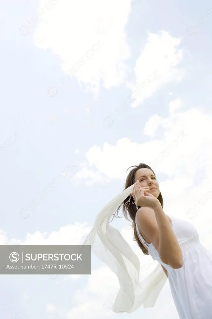 Woman holding up shawl outdoors, tousled by wind, low angle view