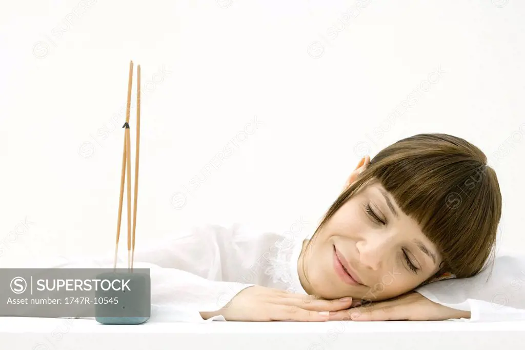 Woman resting head on arm beside incense, smiling with eyes closed