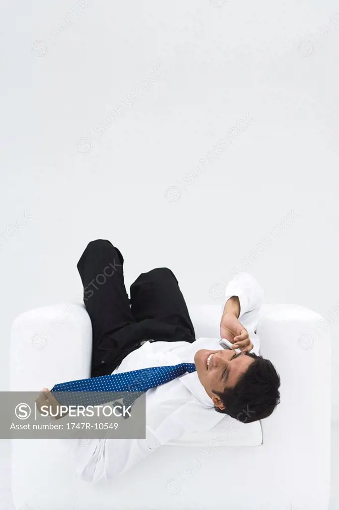 Businessman lying upside down in armchair, talking on the phone