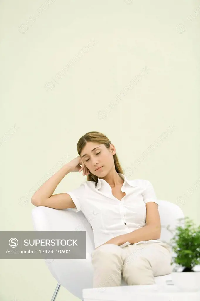 Woman sitting in chair, leaning against elbow, eyes closed