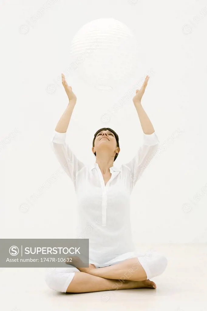 Woman sitting cross-legged on the ground with arms raised, looking up at sphere