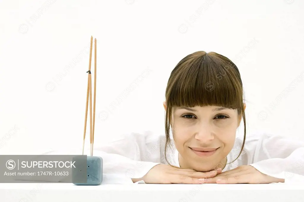 Woman resting head on arms beside incense, smiling at camera