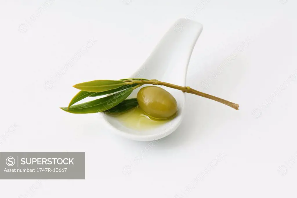 Green olive in spoon, leaf garnish