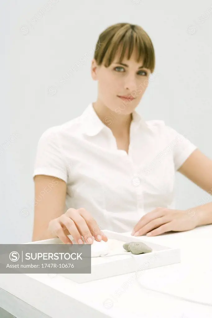 Woman sitting at desk, using computer mouse in small rock garden, smiling at camera