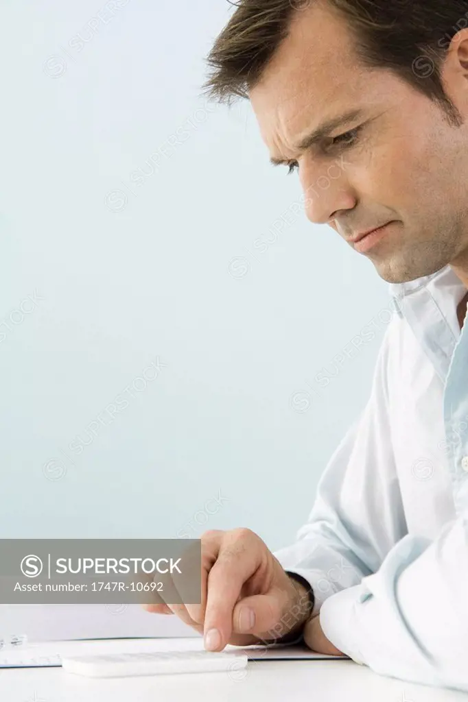 Man using calculator, sitting at table, side view