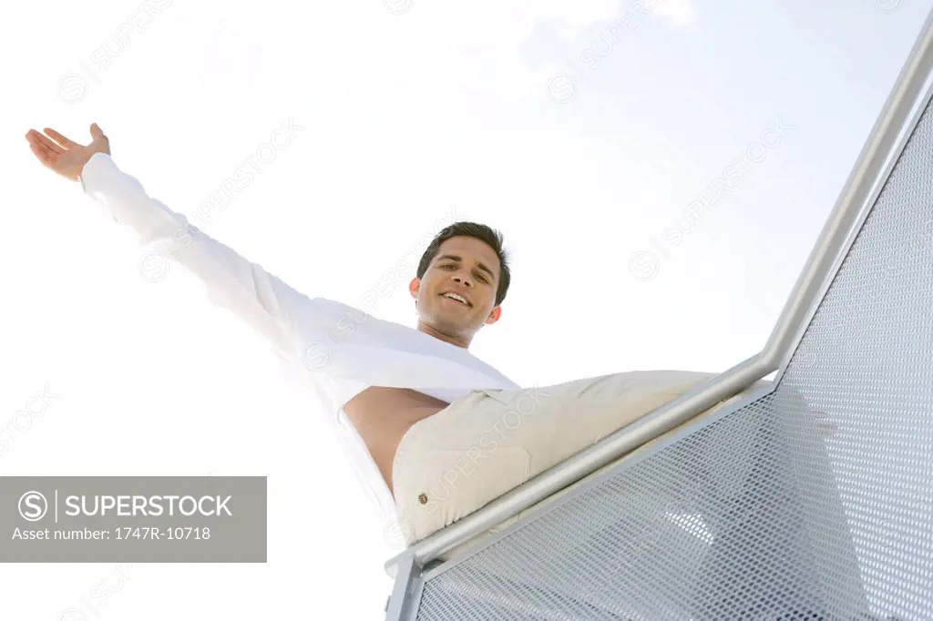 Man sitting on balcony, one arm raised, low angle view