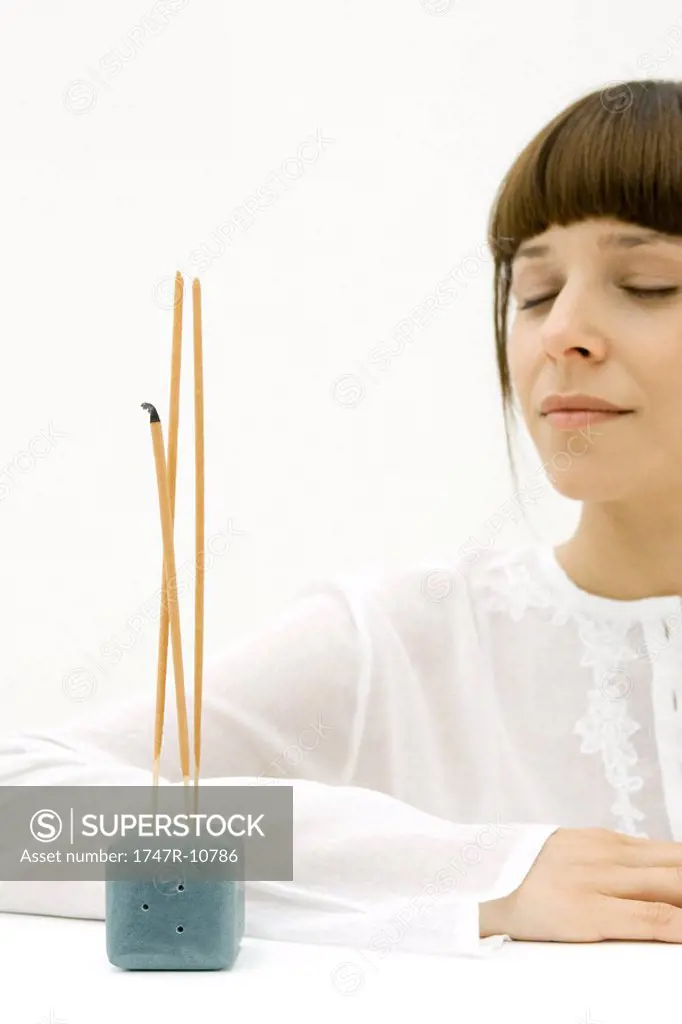 Woman sitting near incense, eyes closed