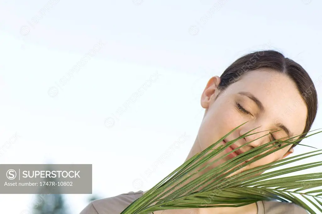 Portrait of young woman holding palm frond, eyes closed