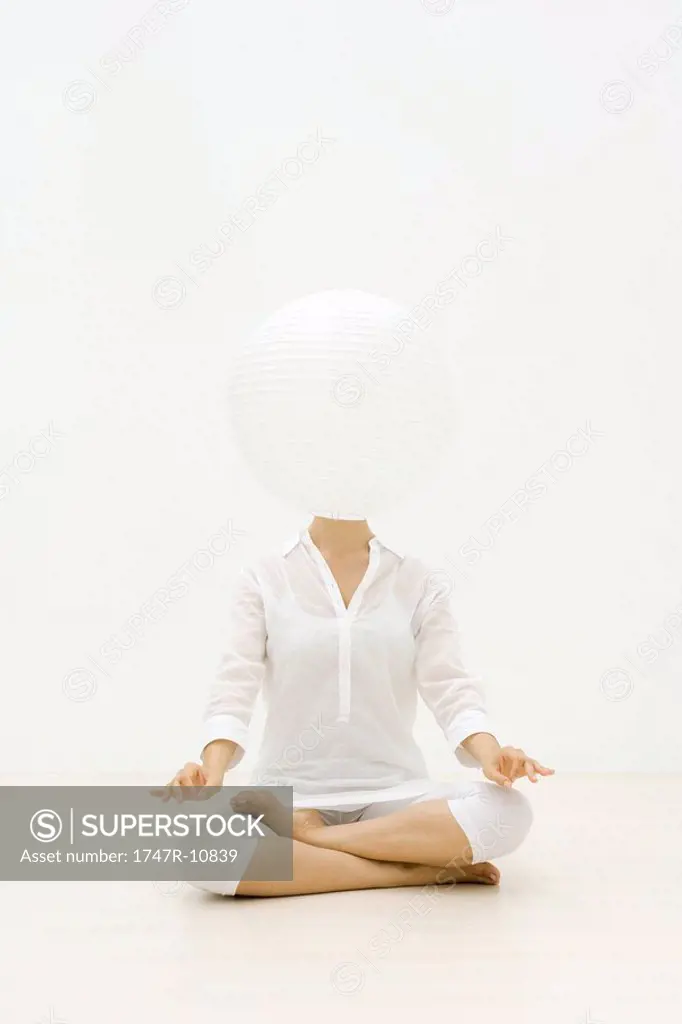 Woman sitting in lotus position, paper lantern obscuring face