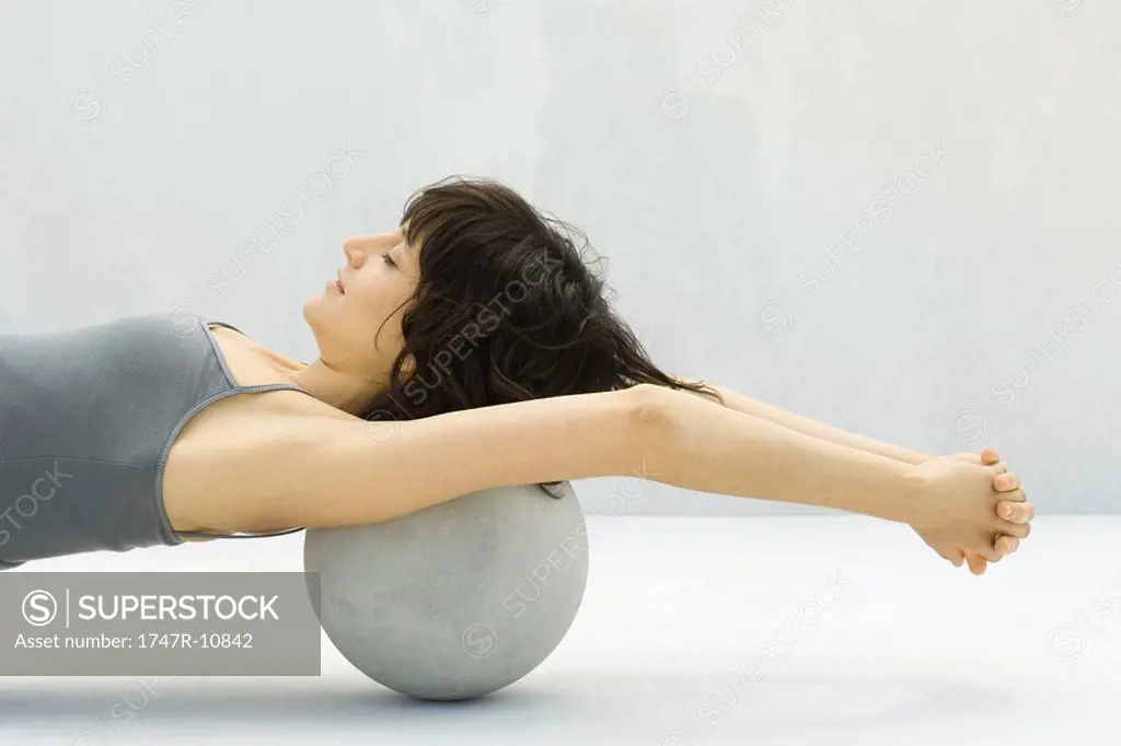 Woman stretching using fitness ball placed at base of head, arms raised