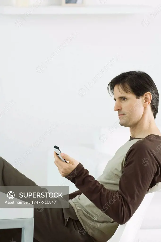 Man holding remote control, sitting and looking away