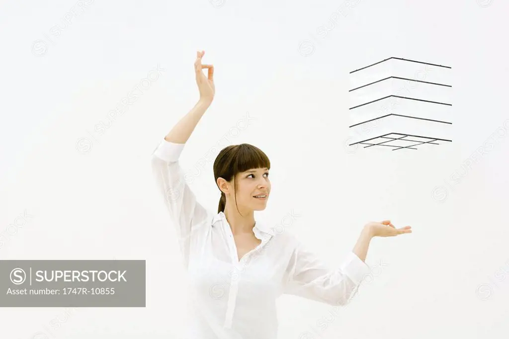 Woman raising arms, looking up at cube floating in midair