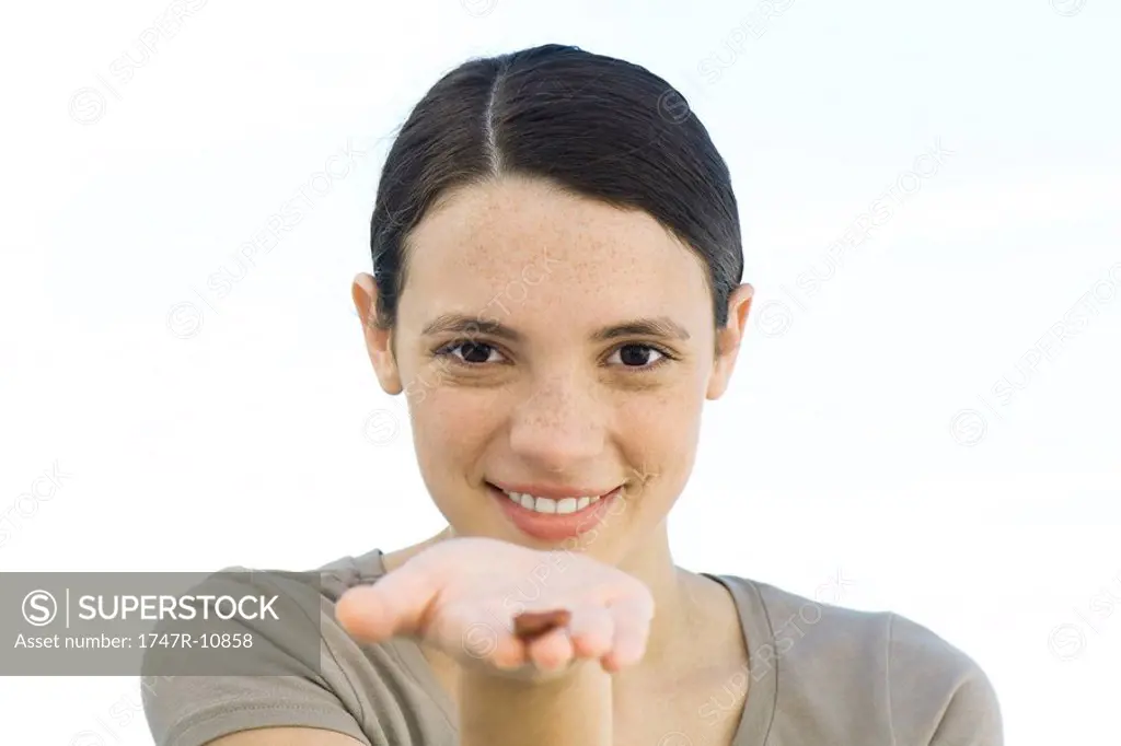Young woman holding single brown seed in palm of hand extended to camera