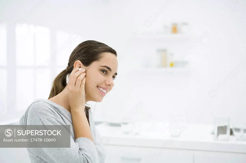 Young female listening to earphones, smiling, looking away