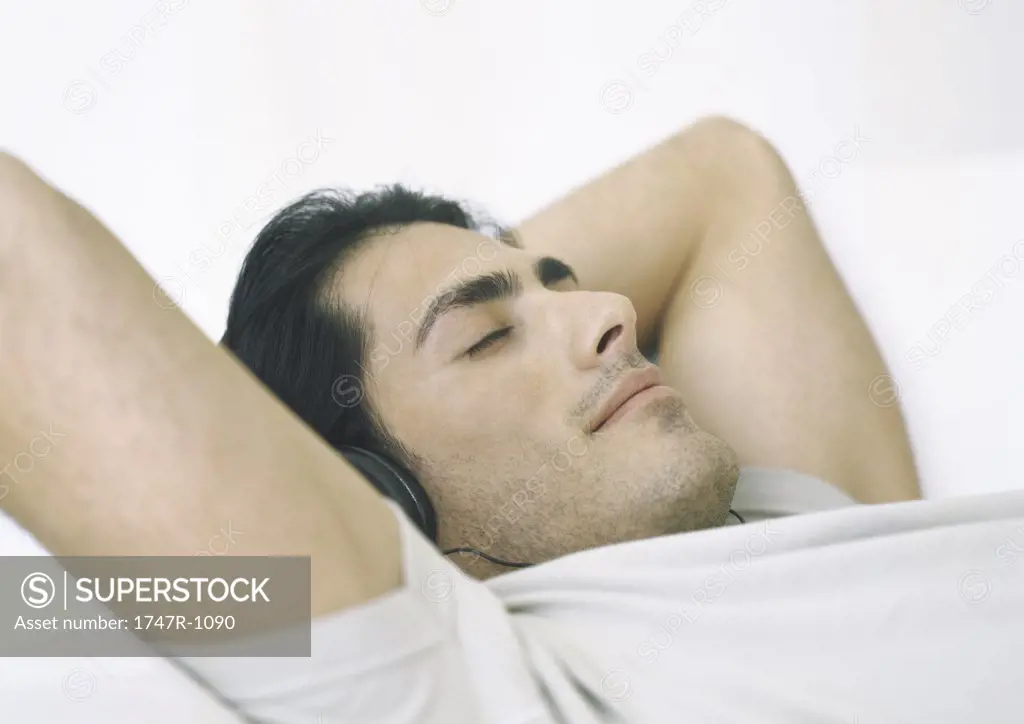 Man lying down, listening to headphones with hands behind head