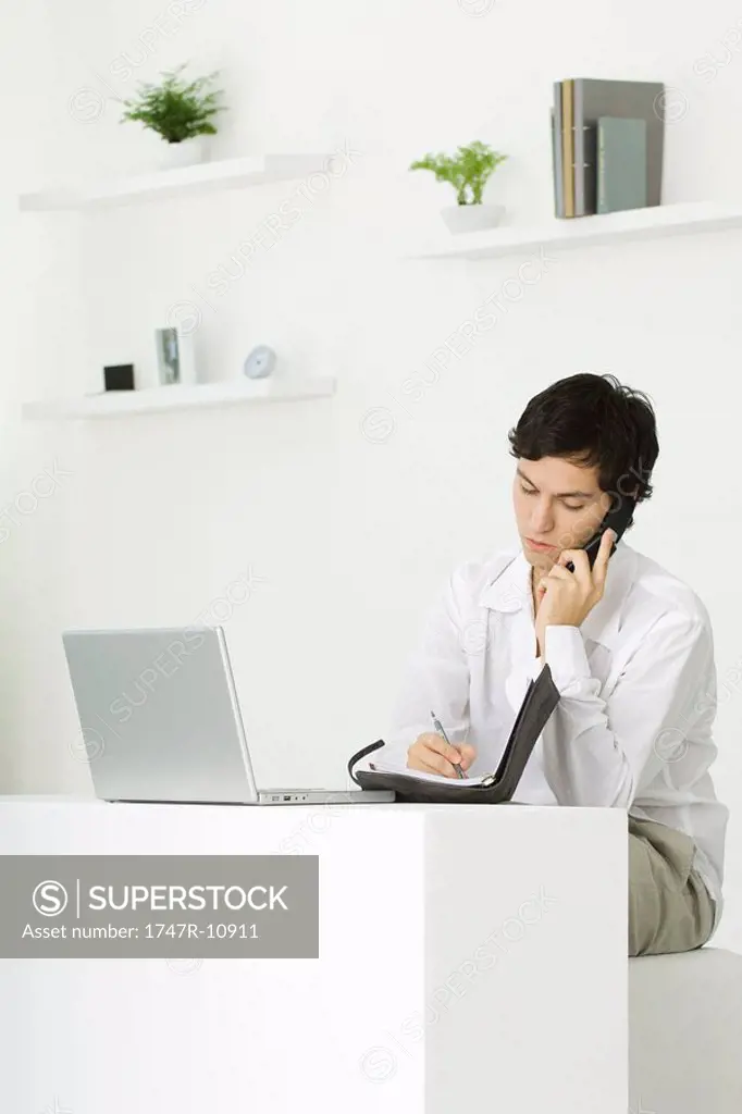 Man sitting at desk talking on landline phone, looking down at agenda