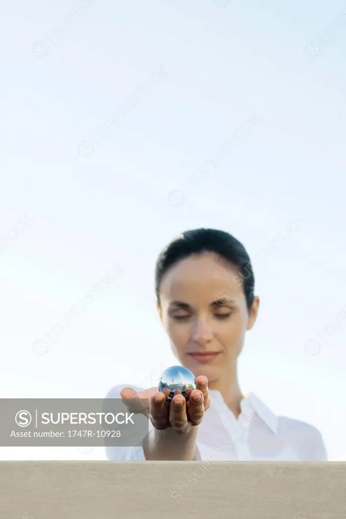 Woman holding out metal sphere, eyes closed