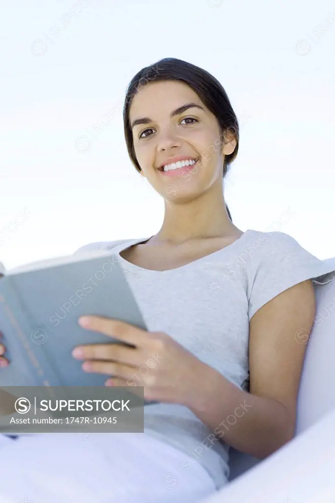 Teenage girl sitting, holding book, smiling at camera