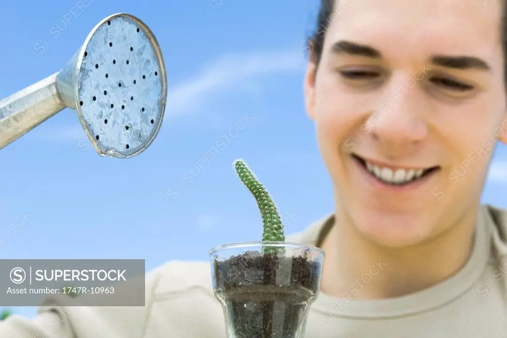 Young man watering small potted cactus