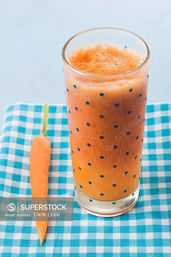 Carrot juice beside a single carrot on tablecloth