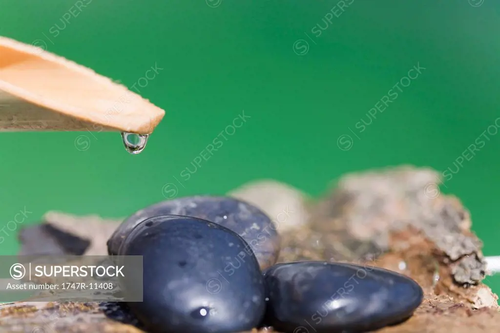 Water droplet hanging off wooden spout over heap of rocks