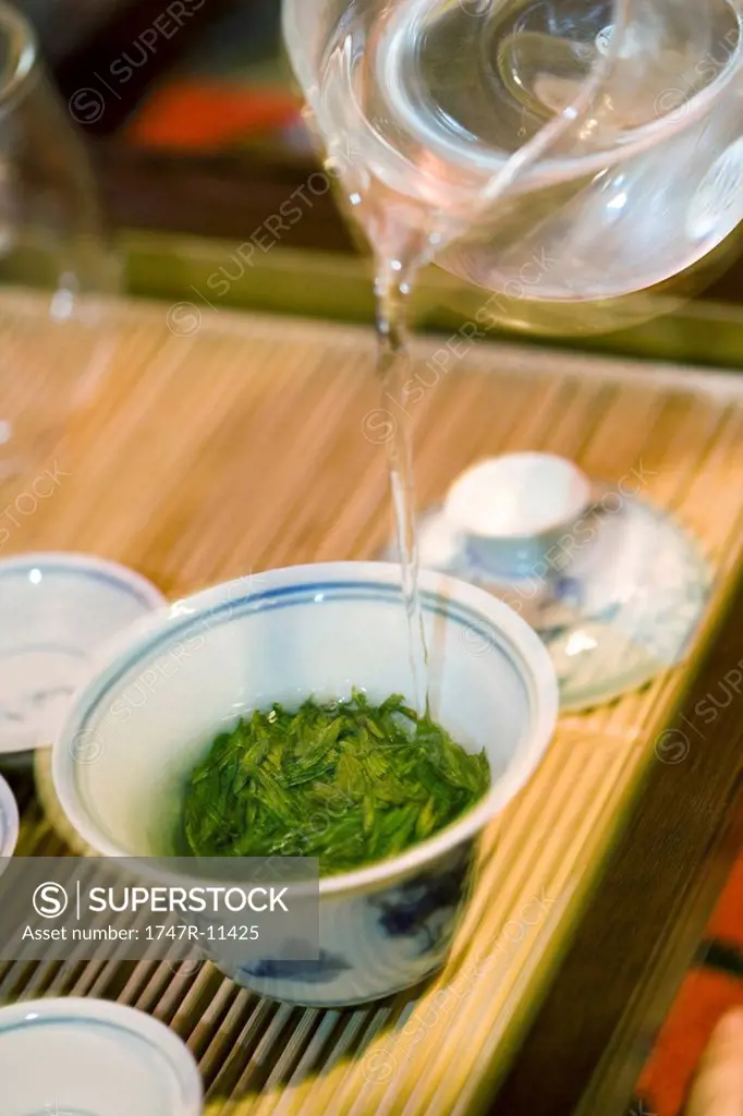 Hot water poured from glass teapot over tea leaves in gaiwan cup