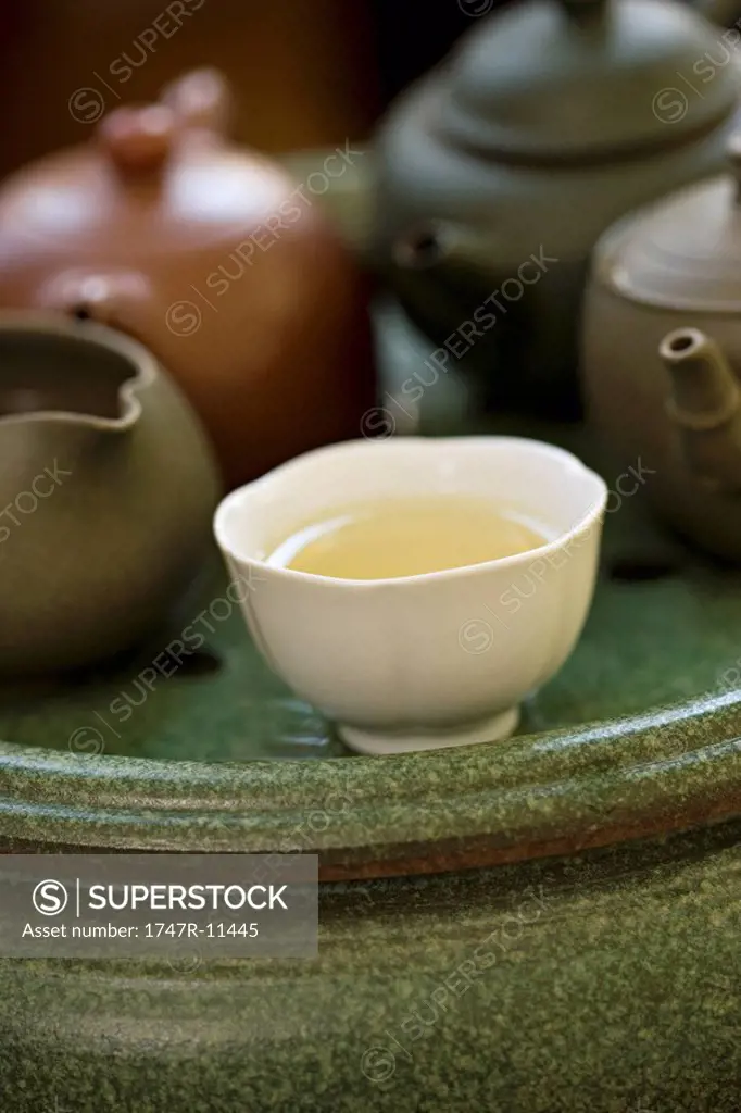 Tea cup full of tea placed before several teapots on tea tray