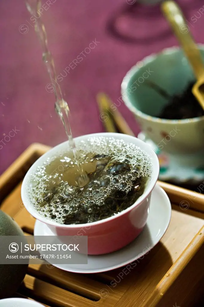 Hot water being poured and splashing over tea leaves in tea cup