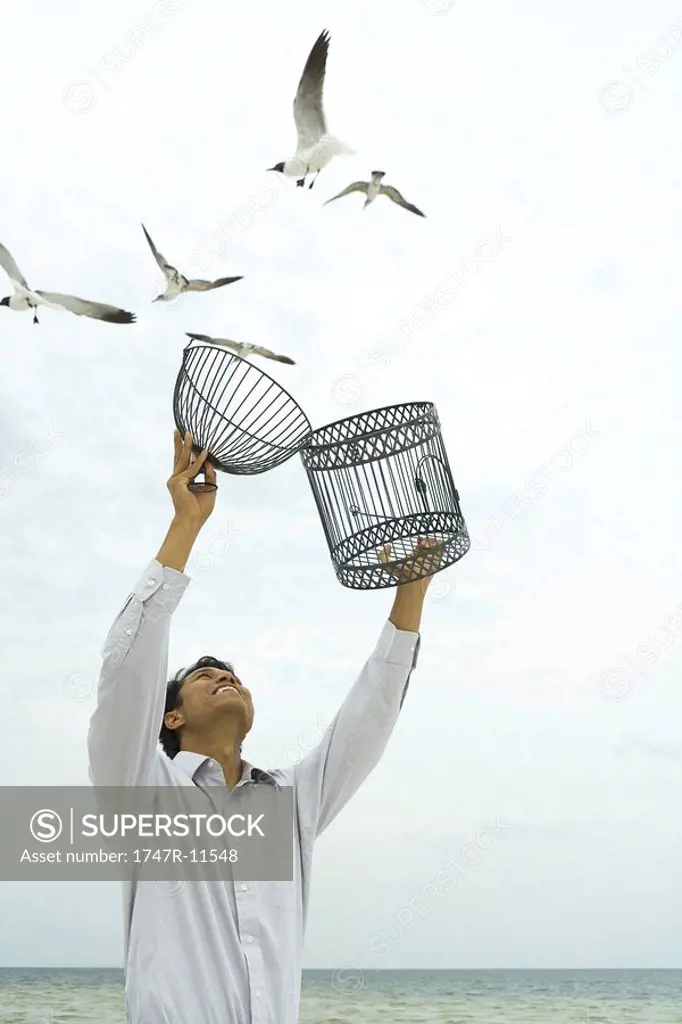 Man releasing bird outdoors, open cage in hand