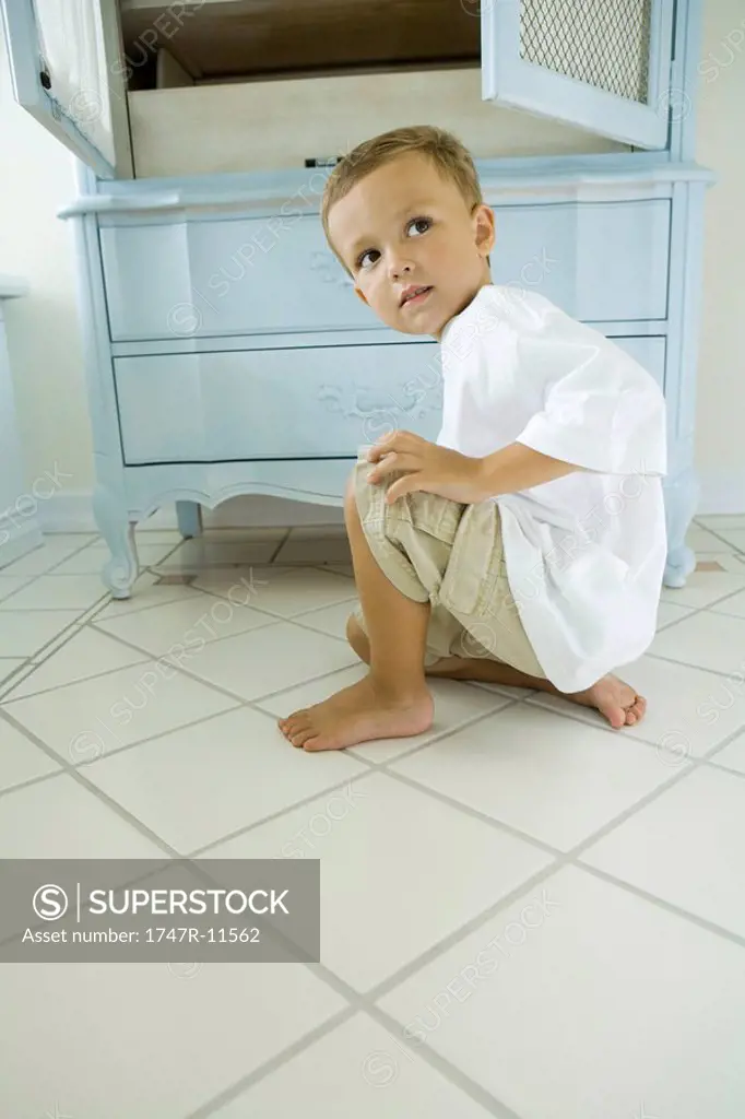 Boy crouching beside open armoire, looking over shoulder
