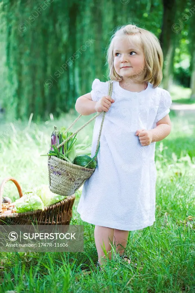 Little girl holding basket of vegetables, looking away
