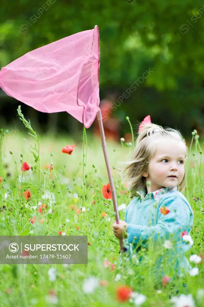 Girl holding up butterfly net, standing in field of flowers