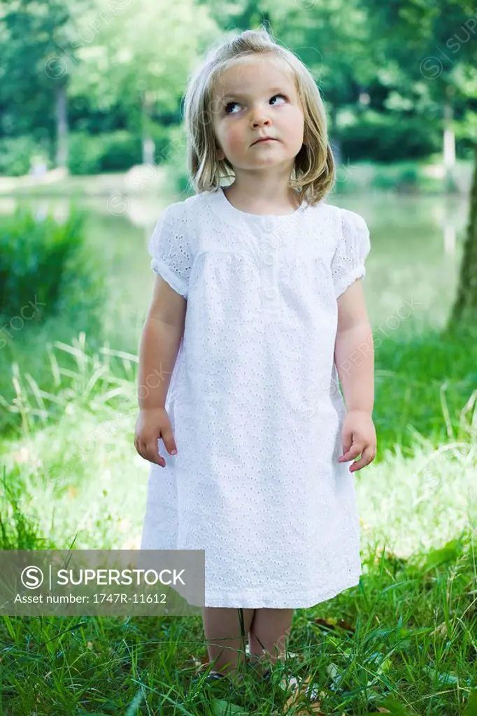 Little girl standing on grass, looking up