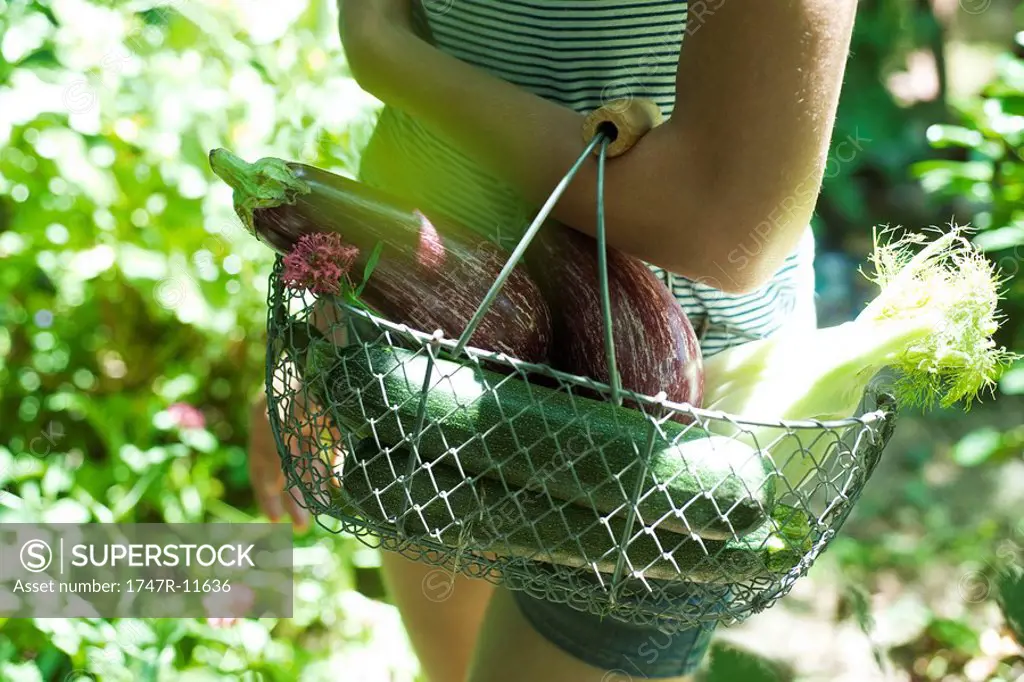 Teenage girl carrying wire basket of vegetables