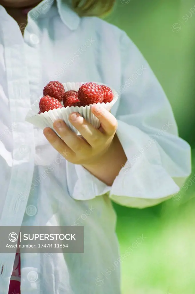 Little girl holding cupcake wrapper full of raspberries, cropped