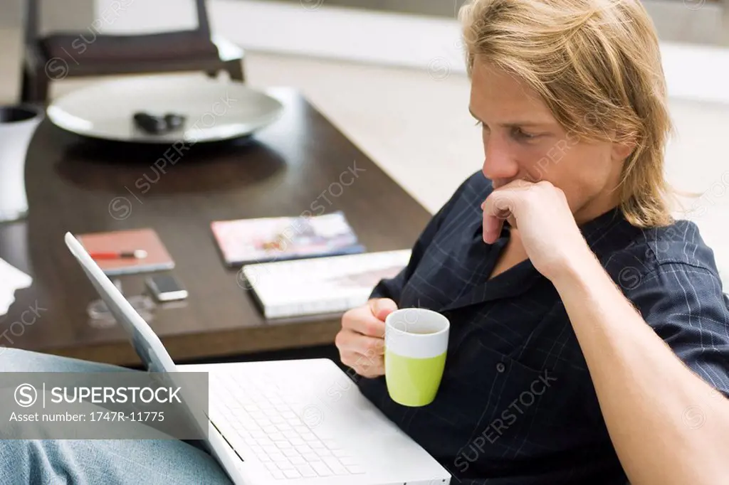 Man on sofa with laptop computer and cup of coffee