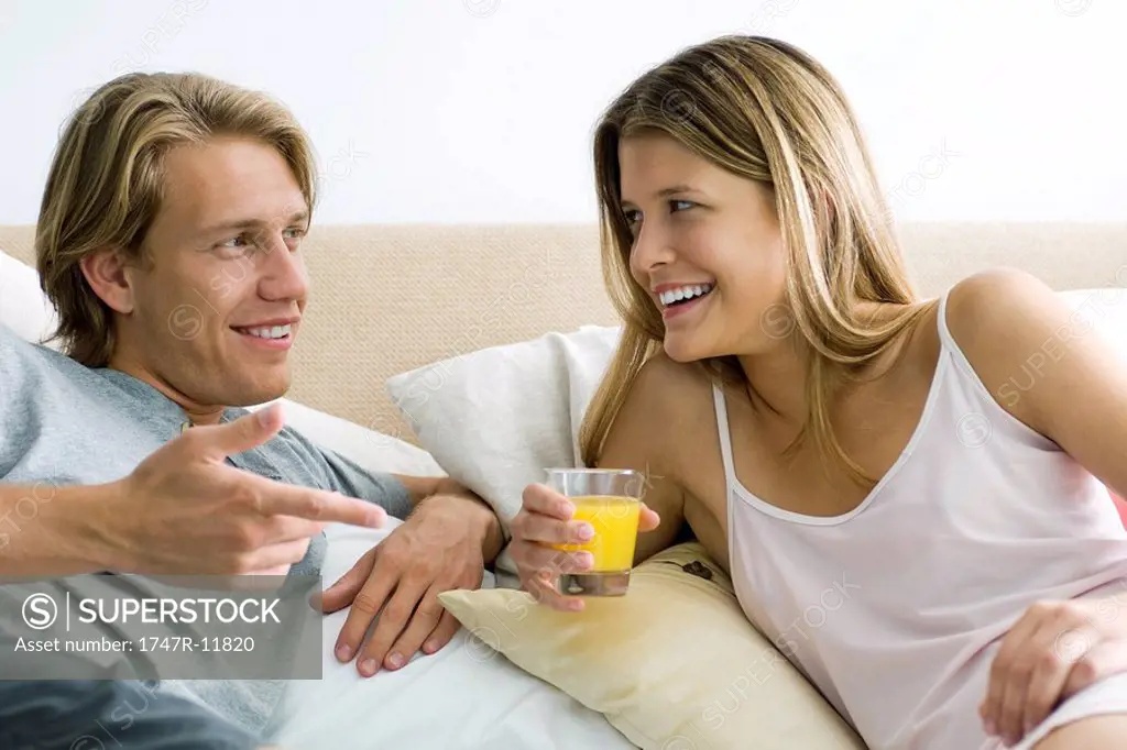 Couple talking together in bed, woman holding glass of orange juice