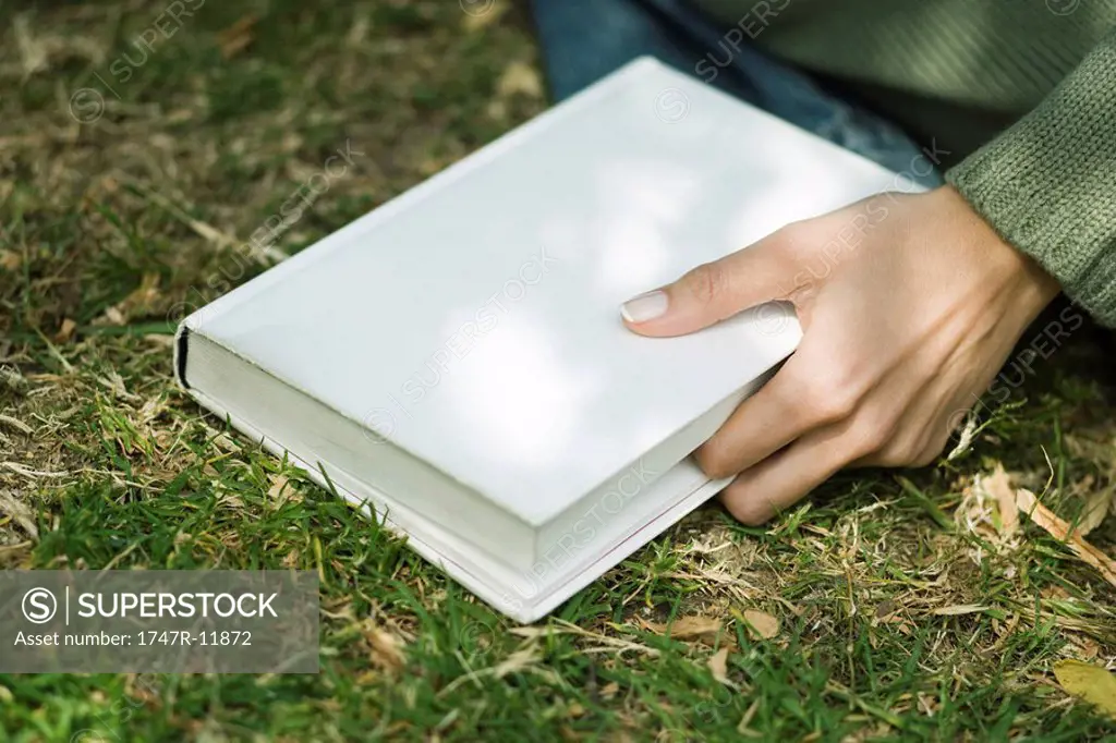 Woman holding closed book, marking place with finger